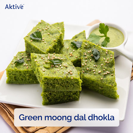 Green moong dal dhokla cubes arranged on a white dish with a bowl of chutney.