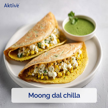 A plate of two moong dal chillas with paneer stuffing with green chutney on the side. 